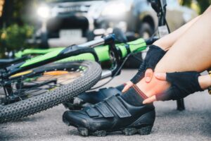 Cropped shot of a female cyclist suffering from ankle pain after a car accident on the road. Concept of car and bicycle collision.