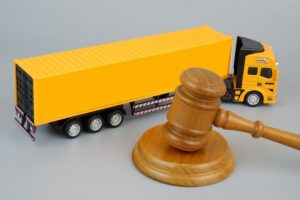 Wooden gavel and yellow cargo truck on a grey background. Concept of laws and transportation. 