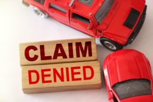 Claim denied words on wooden blocks and two red cars in road accident on white