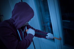 Hooded housebreaker forcing window lock to make a theft in a house at night
